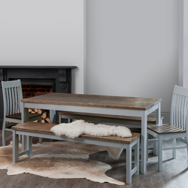A grey dining table with dark pine wood tabletop accompanied by matching chairs and a bench, set in a room with a fireplace.