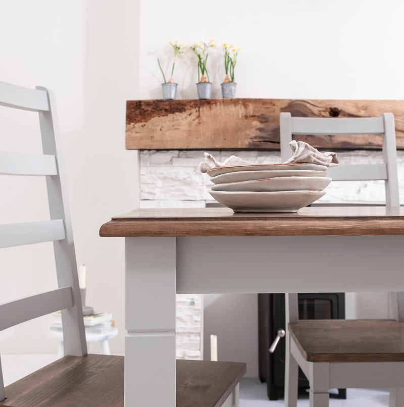 Dining table with wooden top and white legs, surrounded by chairs in a bright room.
