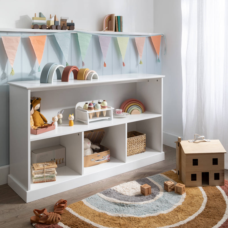 A white Halmstad 3 Cube & Shelf Storage Unit with various children's toys and books displayed on the shelves and in the cubes, placed in a room with a round rug, wooden house, and decorative flags on the wall.