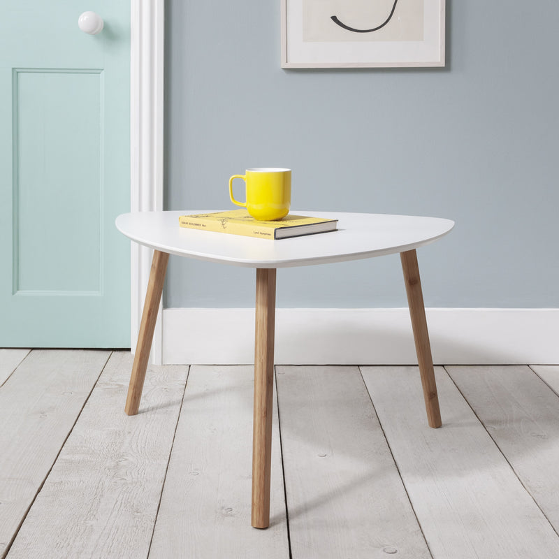 An extra large side table with a white tabletop and natural pine legs, placed on a wooden floor against a wall with a door, with a yellow mug and a book on top of the table.