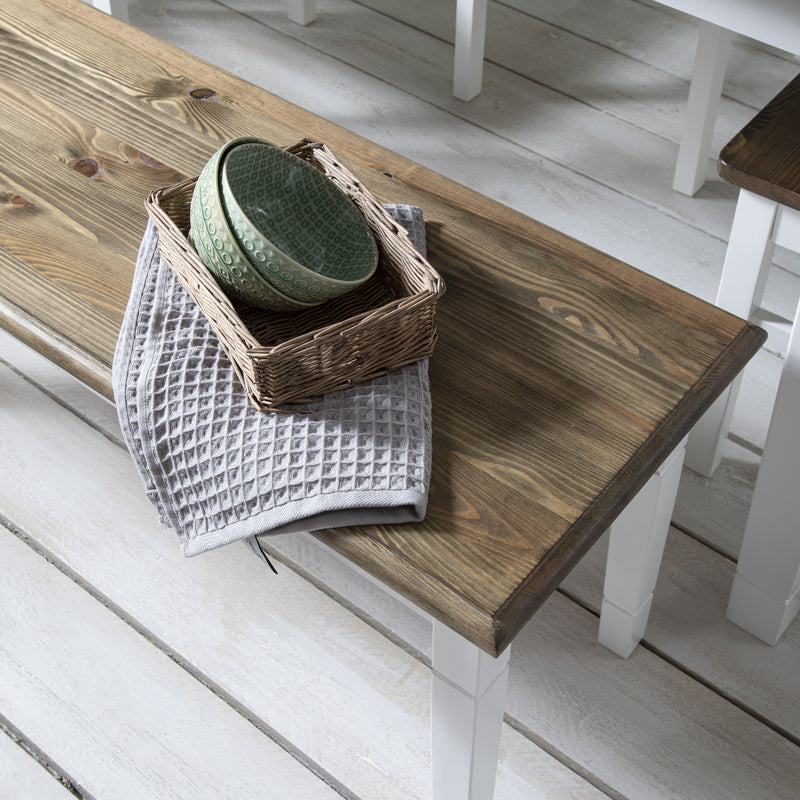 Wooden table with a basket containing a green ceramic bowl and a gray towel on a white wooden floor.