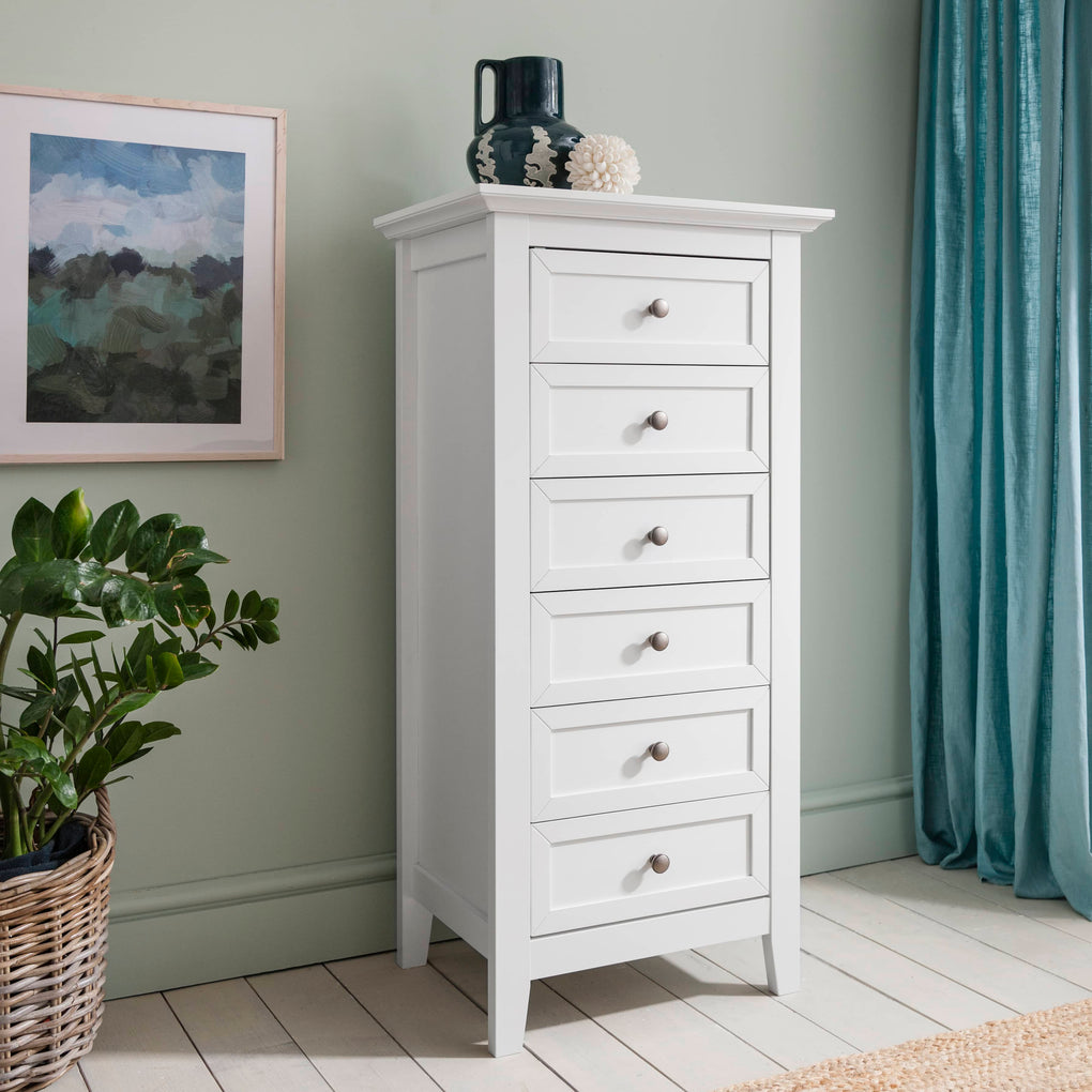 White tall chest of drawers in a room with a plant and framed picture.